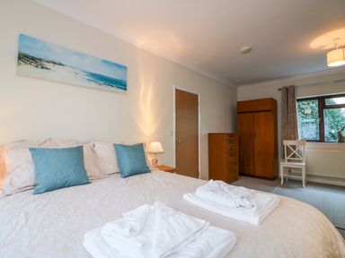 A bedroom with a double bed with blue pillows and white towels a wooden wardrobe and chest of drawers and a window with curtains at Little Waycroft in Dawlish