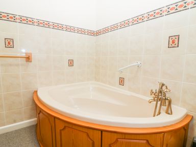 A corner bathtub with wooden paneling and tiled walls with patterned border at Little Waycroft in Dawlish