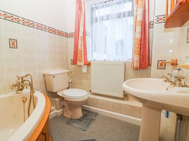 A bathroom with a bathtub toilet and sink under a window with curtains at Little Waycroft in Dawlish