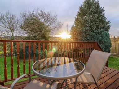 A wooden deck with a glass table and two chairs overlooking trees and grass at Little Waycroft in Dawlish