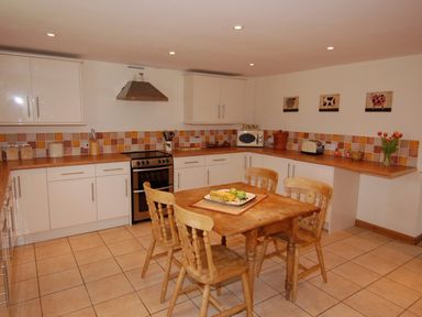 A kitchen with wooden table and chairs a stove microwave and tiled backsplash at West Perry Hay in North Chideock near Chideock