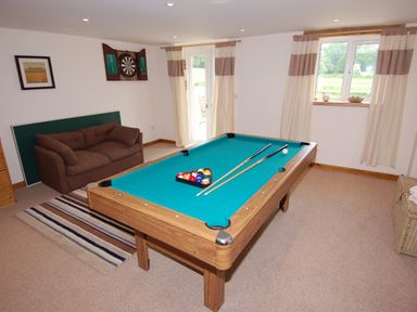 A game room with a pool table couch dartboard and windows at West Perry Hay in North Chideock near Chideock