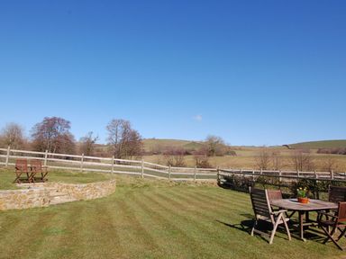 A garden with wooden chairs and table on grass near a stone wall and fenced fields at West Perry Hay in North Chideock near Chideock