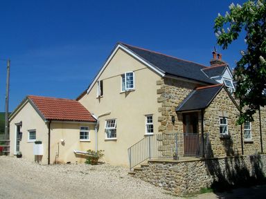 An exterior view of a two story house with stone and plaster walls under a blue sky at West Perry Hay in North Chideock near Chideock