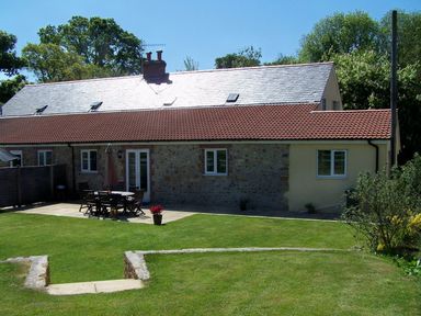 A backyard with lawn and patio furniture outside a stone and tiled roof house at West Perry Hay in North Chideock near Chideock