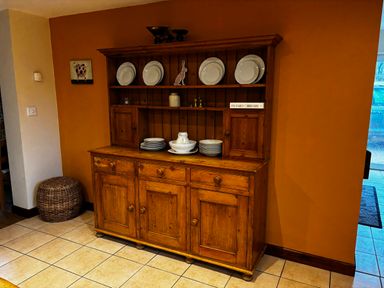 A wooden dresser with plates and bowls on shelves in a room with orange and beige walls at West Perry Hay in North Chideock near Chideock