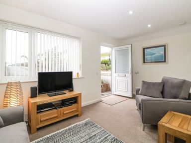 A living room with a television on a wooden stand a gray armchair and an open door at Monkbarns in Brixham