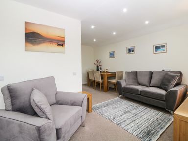 A living room with two gray sofas a patterned rug a wooden dining table with chairs and landscape pictures on the walls at Monkbarns in Brixham
