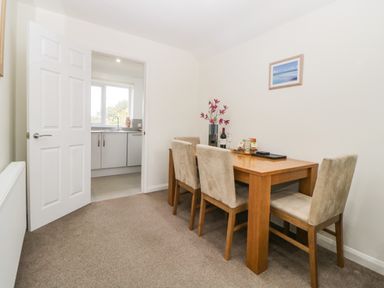 A dining room with a wooden table and four chairs next to an open door leading to a kitchen at Monkbarns in Brixham