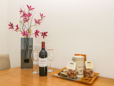 A table with a vase of pink flowers a bottle of red wine two wine glasses and a tray of biscuits and fudge at Monkbarns in Brixham