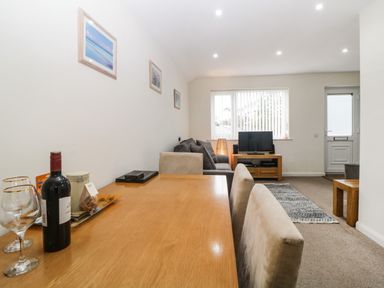 A dining table with wine and glasses in a living room with a sofa and a television at Monkbarns in Brixham