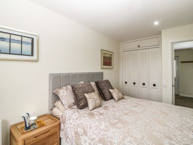 A bedroom with a bed and pillows a wooden nightstand with items and multiple closets at Monkbarns in Brixham