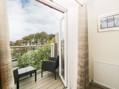A balcony with two chairs and a table overlooking trees at Monkbarns in Brixham