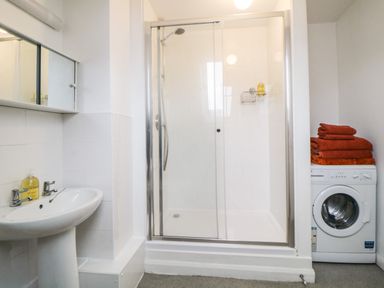 A bathroom with a shower enclosure a sink washing machine and towels stacked on the washing machine at Monkbarns in Brixham