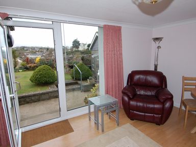 A room with a leather armchair glass tables and a door opening to a garden at Garden View in Kingskerswell