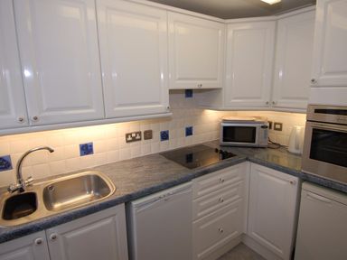 A kitchen with a sink, white cabinets, a microwave, an oven, and a stove at Garden View in Kingskerswell