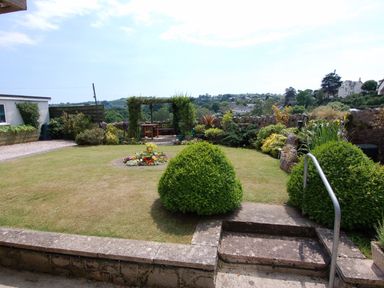 A garden with a lawn a flower bed shrubs stone steps and a wooden pergola at Garden View in Kingskerswell
