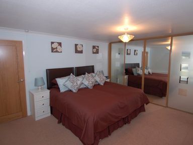 A bedroom with a bed a nightstand and mirrored wardrobes at Garden View in Kingskerswell
