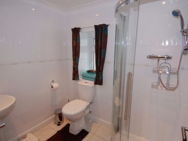 A bathroom with a toilet a shower with glass door and a window with curtains at Garden View in Kingskerswell