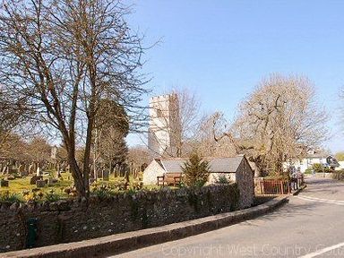 A churchyard with gravestones trees and a stone wall beside a road at Garden View in Kingskerswell