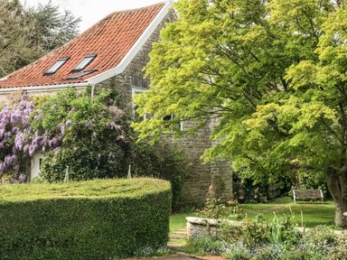 A stone house with a red tiled roof surrounded by trees and shrubs at The Granary Edington near Street and Glastonbury