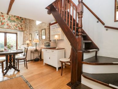 A dining area with a round table and chairs next to a wooden staircase and a white cabinet with a microwave at The Granary Edington near Street and Glastonbury