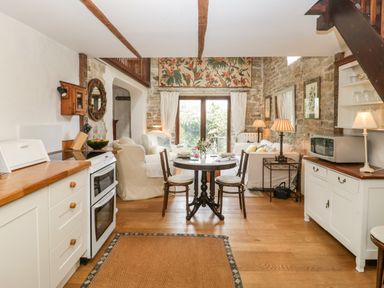 A kitchen and living area with wooden floor a round dining table and chairs white sofas and stone walls at The Granary in Edington near Street and Glastonbury
