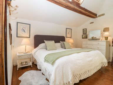 A bedroom with a double bed white bedding green throw pillows bedside tables with lamps a dresser with mirror and wooden beams on ceiling at The Granary in Edington near Street and Glastonbury