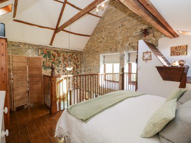 A bedroom with a bed, wooden floor, stone wall, wooden beams and a folding screen at The Granary in Edington near Street and Glastonbury