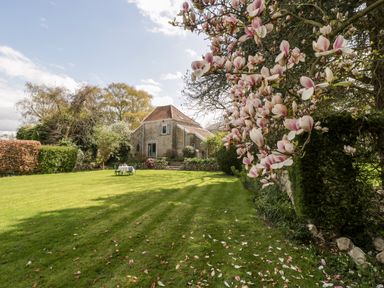 A garden with a lawn table and chairs near a stone house and blossoming tree branches at The Granary in Edington near Street and Glastonbury
