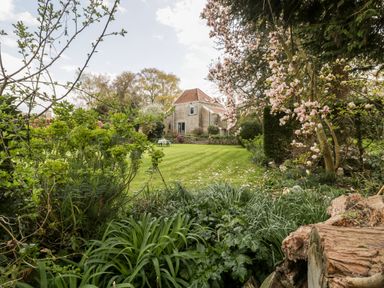 A garden with a lawn trees shrubs and a stone house in the background at The Granary in Edington near Street and Glastonbury