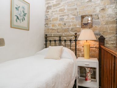 A bedroom with a bed and white bedding next to a bedside table with a yellow lamp and a decorative jug at The Granary in Edington near Street and Glastonbury