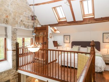 A bedroom loft with a bed table lamps wooden floor and stone wall at The Granary in Edington near Street and Glastonbury
