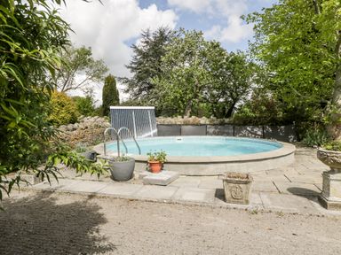 An outdoor circular swimming pool surrounded by stone tiles and potted plants at The Granary in Edington near Street and Glastonbury