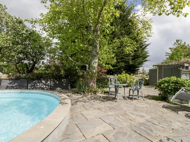 A garden patio with a round swimming pool table and two chairs under a tree at The Granary in Edington near Street and Glastonbury