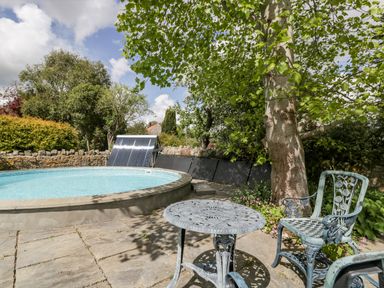 An outdoor patio with a round metal table and chairs next to a round swimming pool and trees at The Granary in Edington near Street and Glastonbury