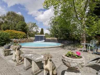 An outdoor patio area with a round pool stone bench with dog statues flower pots and metal table and chairs at The Granary in Edington near Street and Glastonbury