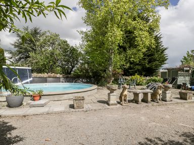 An outdoor area with a round pool stone statues of dogs stone planters and patio furniture at The Granary in Edington near Street and Glastonbury