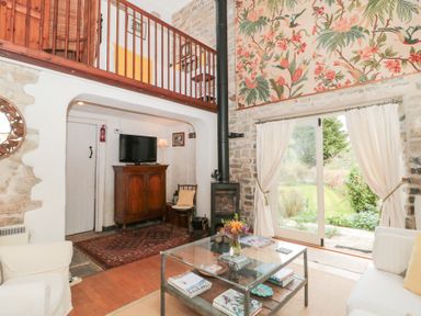 A living room with a glass coffee table flowers on the table wooden cabinet television wood burner and stairs to a mezzanine at The Granary in Edington near Street and Glastonbury