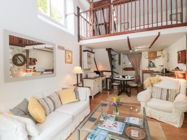 A living room with sofa armchair glass coffee table dining area and wooden beams at The Granary in Edington near Street and Glastonbury