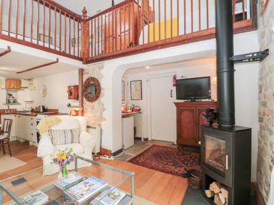 A living area with a glass coffee table flowers on the table white armchair wooden staircase and black wood stove at The Granary in Edington near Street and Glastonbury
