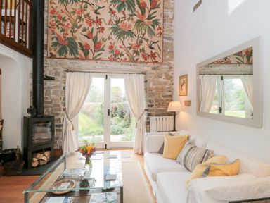 A living room with a white sofa and yellow cushions glass coffee table and wood burning stove at The Granary in Edington near Street and Glastonbury