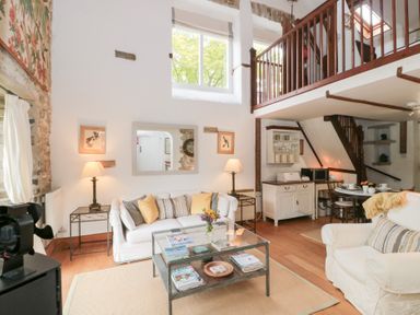 A living room with white sofas a glass coffee table lamps and a dining area with stairs and loft at The Granary in Edington near Street and Glastonbury