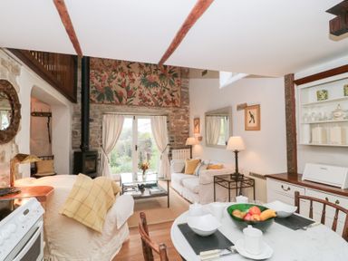 A living room and kitchen area with white couches a glass coffee table a round dining table with fruit and a wood burning stove at The Granary in Edington near Street and Glastonbury