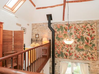 A bedroom loft with a metal bed frame yellow bedding and a wicker room divider at The Granary in Edington near Street and Glastonbury