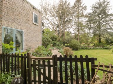 A garden view with a wooden gate stone house wall and green lawn at The Granary in Edington near Street and Glastonbury