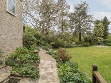 A garden path beside a stone house with plants trees and a lawn at The Granary in Edington near Street and Glastonbury