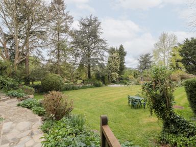 A garden with lawn and outdoor table with chairs surrounded by trees and plants at The Granary in Edington near Street and Glastonbury
