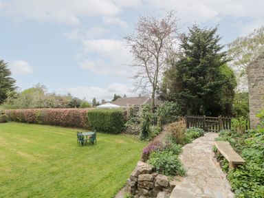 A garden with a stone pathway bench and table with chairs surrounded by shrubs and trees at The Granary in Edington near Street and Glastonbury