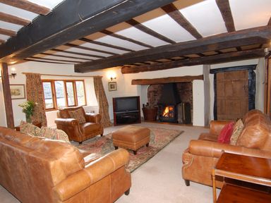 A living room with leather sofas and armchairs a television and a fireplace at Surridge Farmhouse in Waterrow